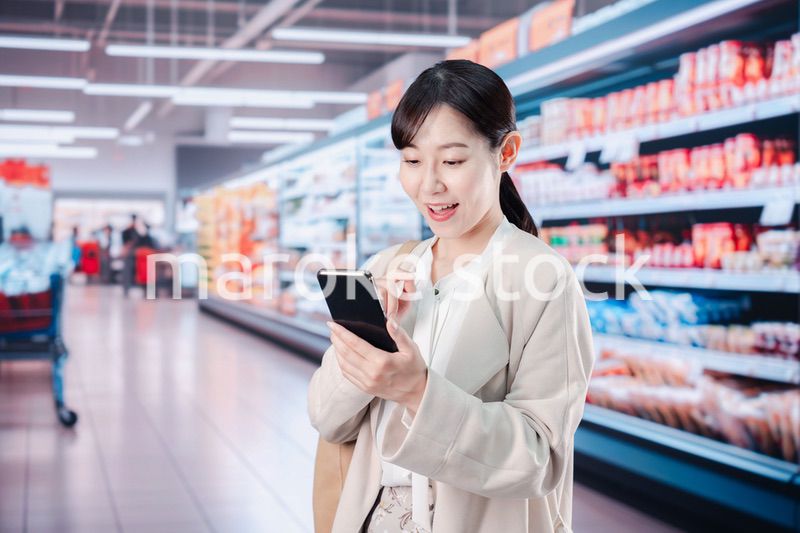 スマホを使いながらスーパーで買い物をする主婦