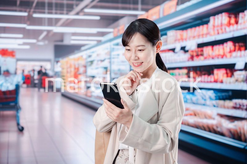 スマホを使いながらスーパーで買い物をする主婦