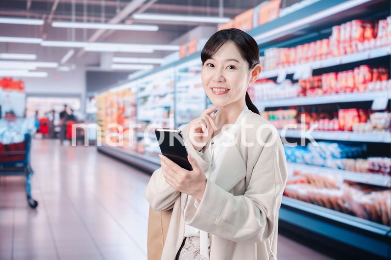 スマホを使いながらスーパーで買い物をする主婦