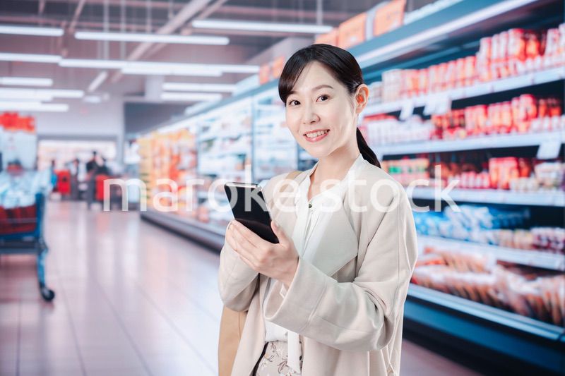 スマホを使いながらスーパーで買い物をする主婦