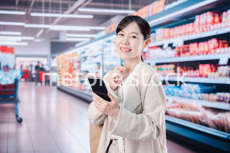 スマホを使いながらスーパーで買い物をする主婦