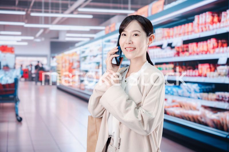 スマホを使いながらスーパーで買い物をする主婦