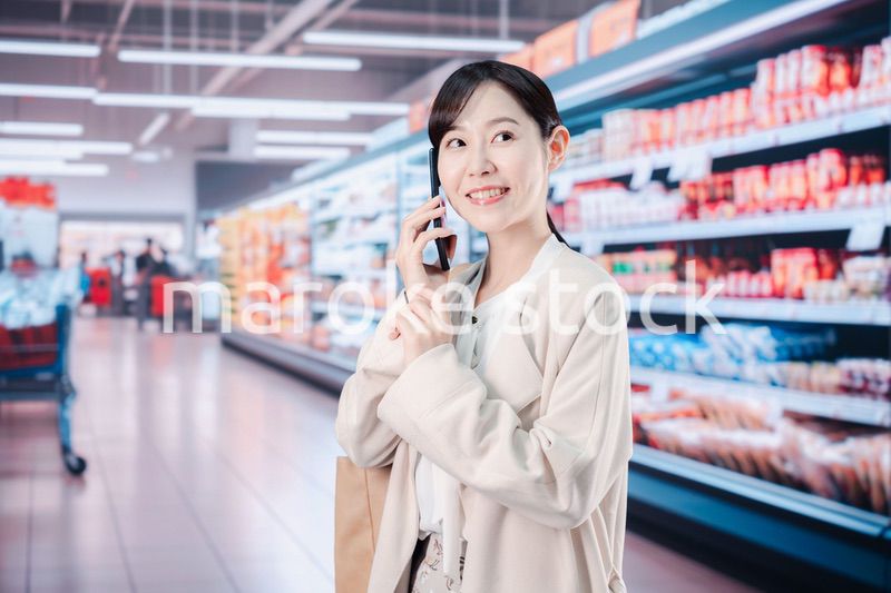 スマホを使いながらスーパーで買い物をする主婦