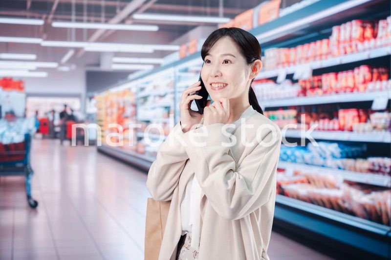 スマホを使いながらスーパーで買い物をする主婦