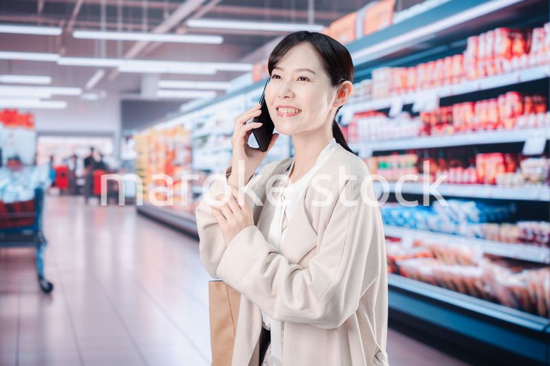 スマホを使いながらスーパーで買い物をする主婦