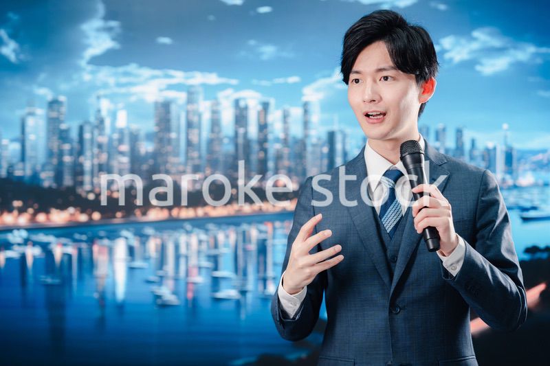 野外でマイクを使って話すスーツを着た男性
