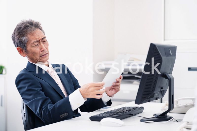 老眼で書類が見づらい高齢のビジネスマン