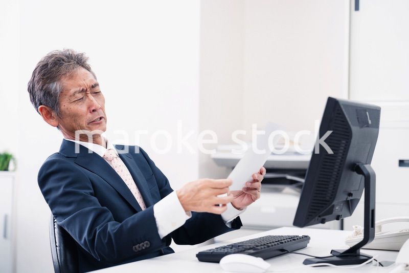 老眼で書類が見づらい高齢のビジネスマン