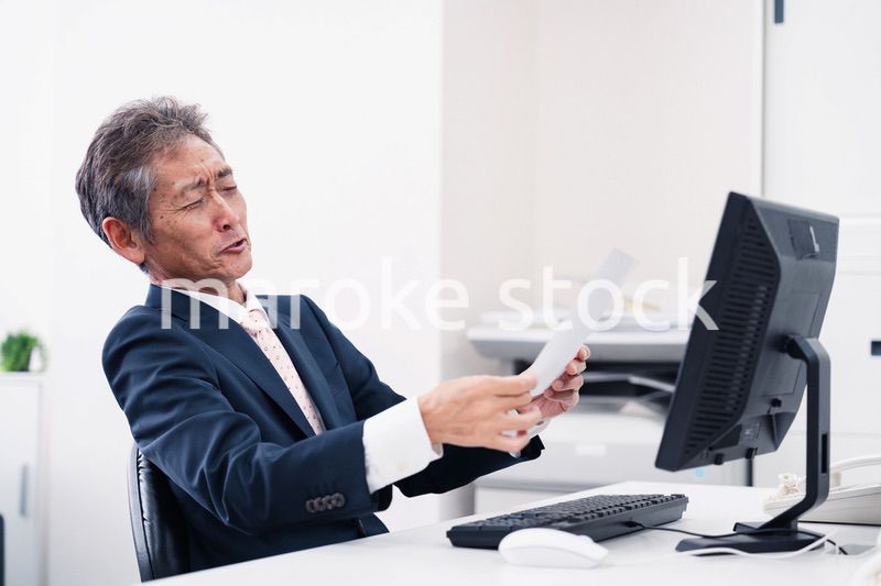 老眼で書類が見づらい高齢のビジネスマン