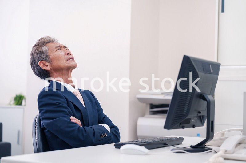 オフィスで腕を組んで悩む中年の上司