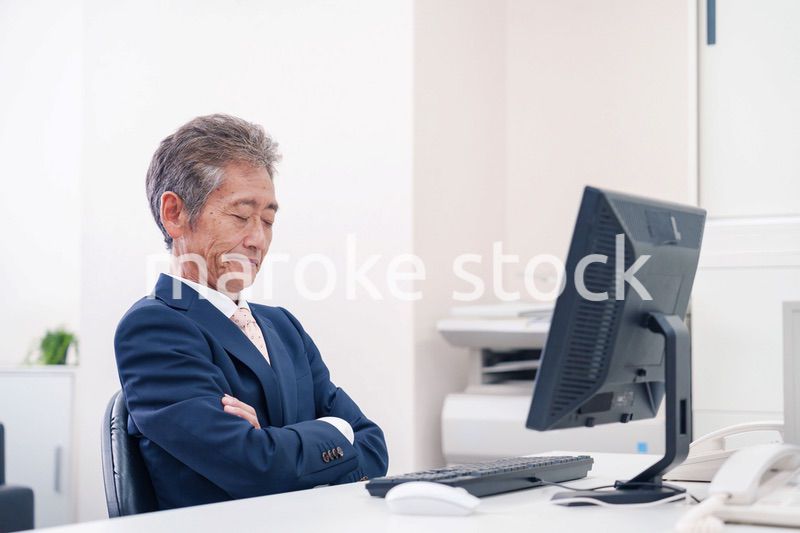 オフィスで腕を組んで悩む中年の上司