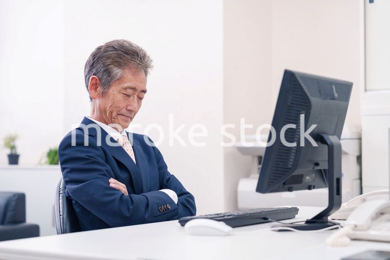 オフィスで腕を組んで悩む中年の上司