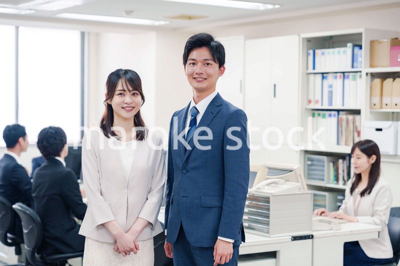 オフィスで笑顔でカメラ目線の男女のビジネスパーソン