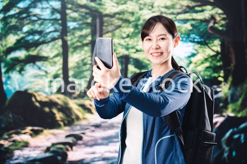 ハイキングをしながらスマホで写真を撮る若い女性