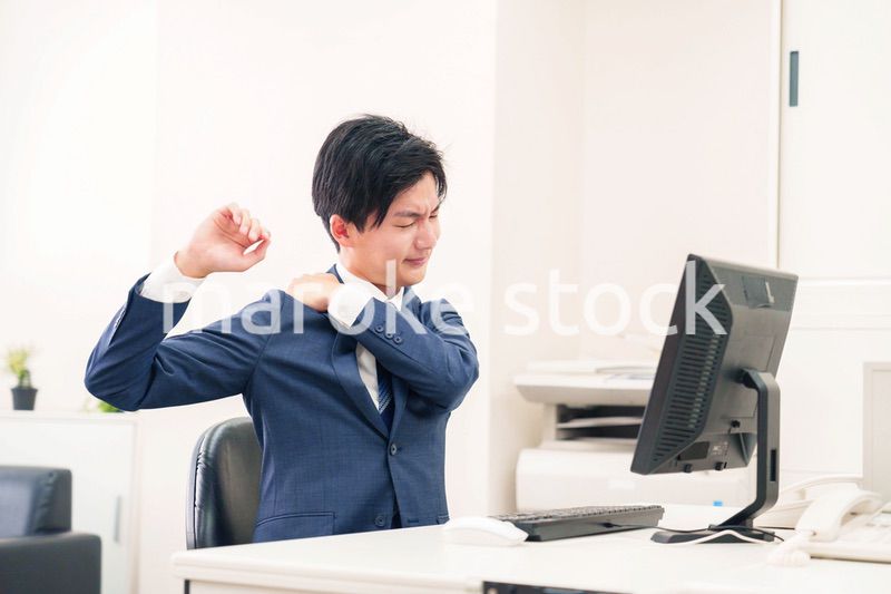 オフィスで肩こりに悩むビジネスマン