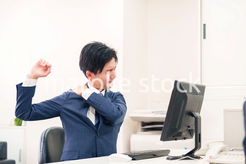 オフィスで肩こりに悩むビジネスマン
