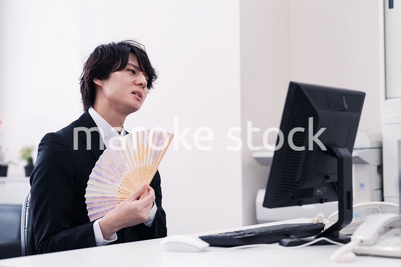 扇子で扇ぎながら仕事をするビジネスマン