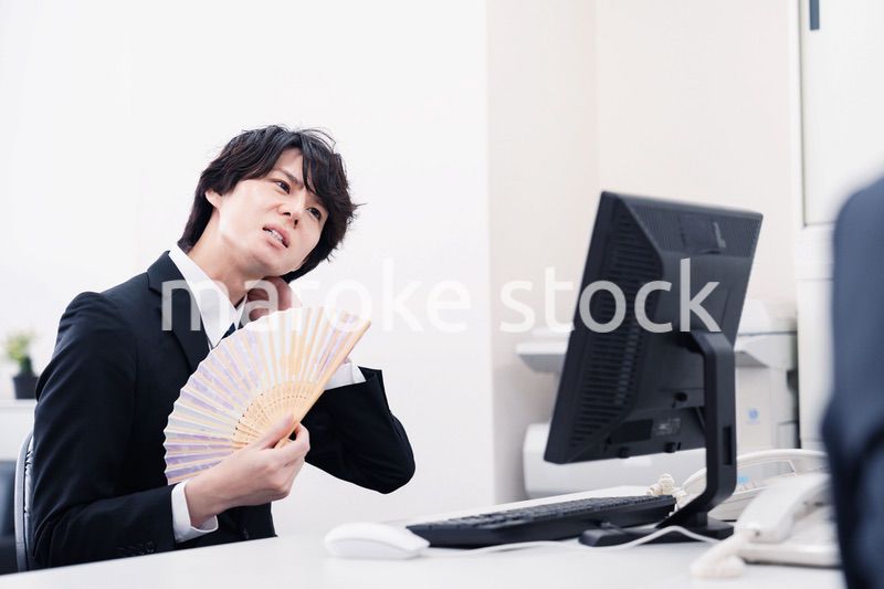 扇子で扇ぎながら仕事をするビジネスマン