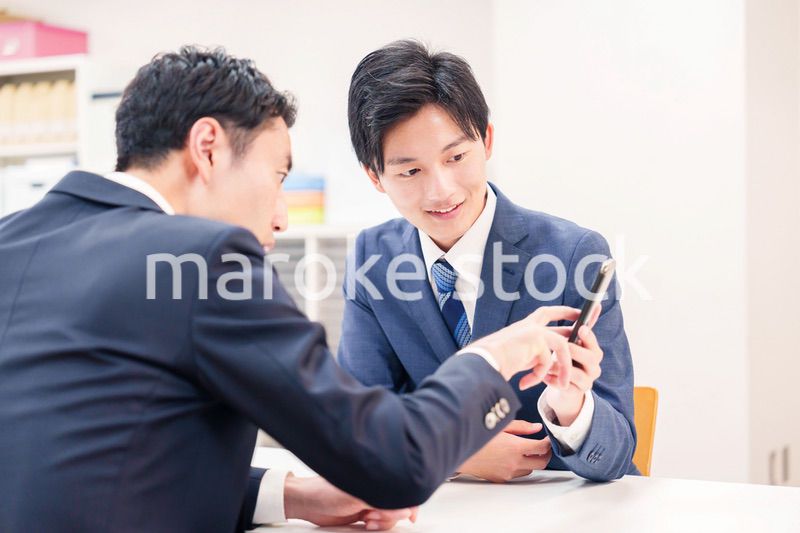 スマホを持って話をする二人のビジネスマン