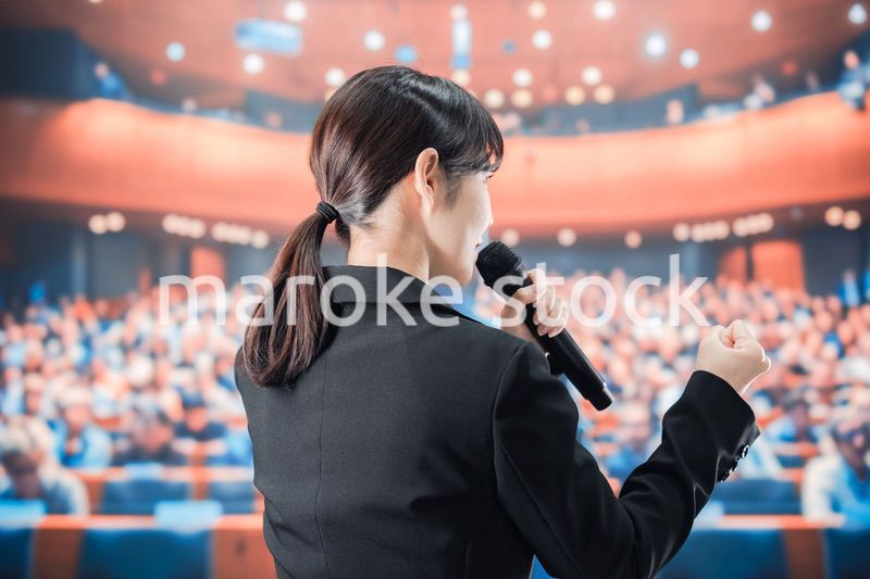 大勢の前でマイクで話す女性