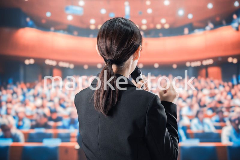 大勢の前でマイクで話す女性