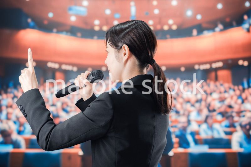 大勢の前でマイクで話す女性