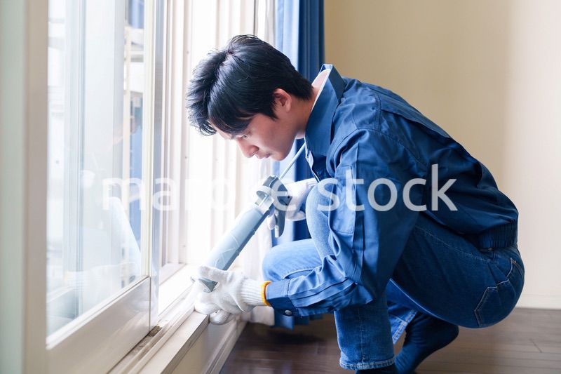 窓にコーキング材を塗る男性の作業員