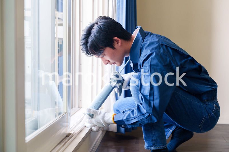 窓にコーキング材を塗る男性の作業員
