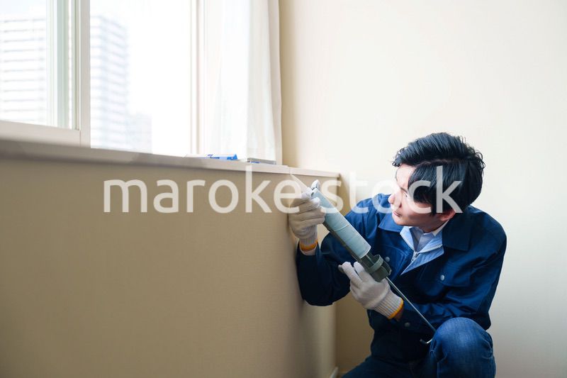 窓にコーキング材を塗る男性の作業員