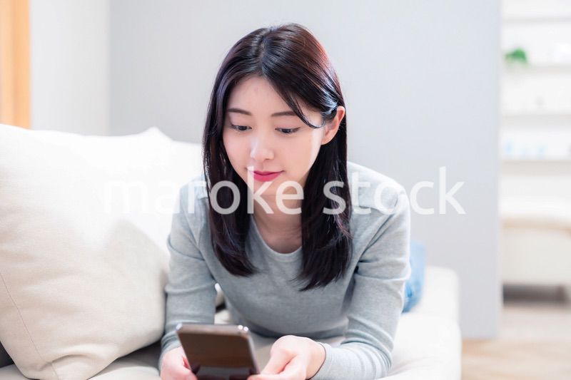 ソファでリラックスをしてスマホを使う若い女性