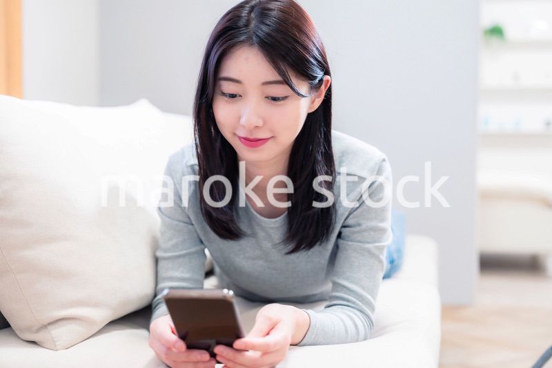 ソファでリラックスをしてスマホを使う若い女性