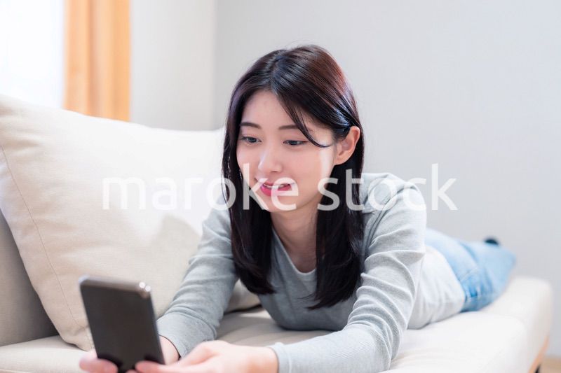 ソファでリラックスをしてスマホを使う若い女性
