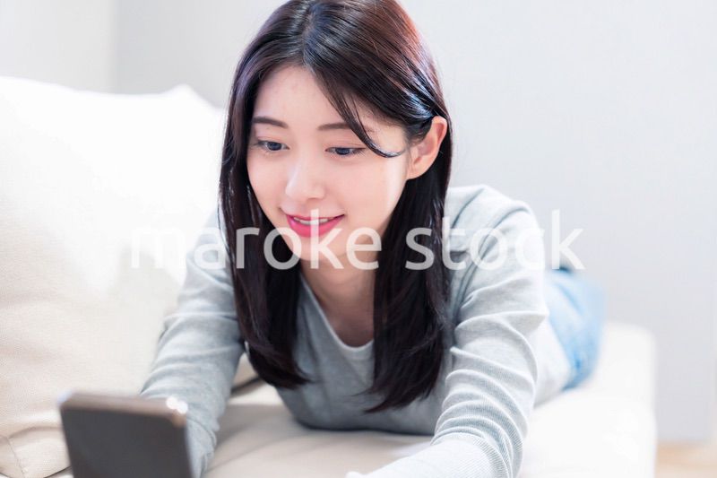 ソファでリラックスをしてスマホを使う若い女性