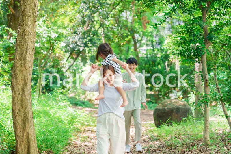 子どもを肩車して森の中を歩く家族