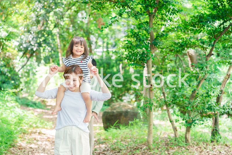 子どもを肩車して森の中を歩く家族