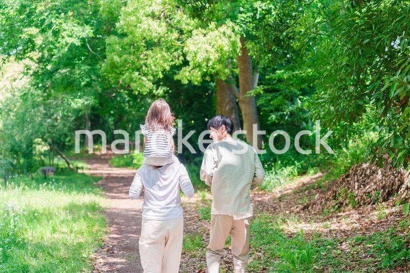 子どもを肩車して森の中を歩く家族