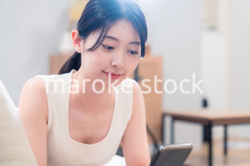 ソファで寝転がってスマホを使う若い女性
