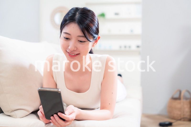 ソファで寝転がってスマホを使う若い女性