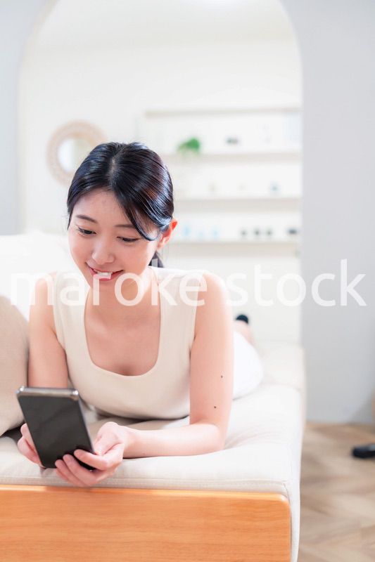 ソファで寝転がってスマホを使う若い女性