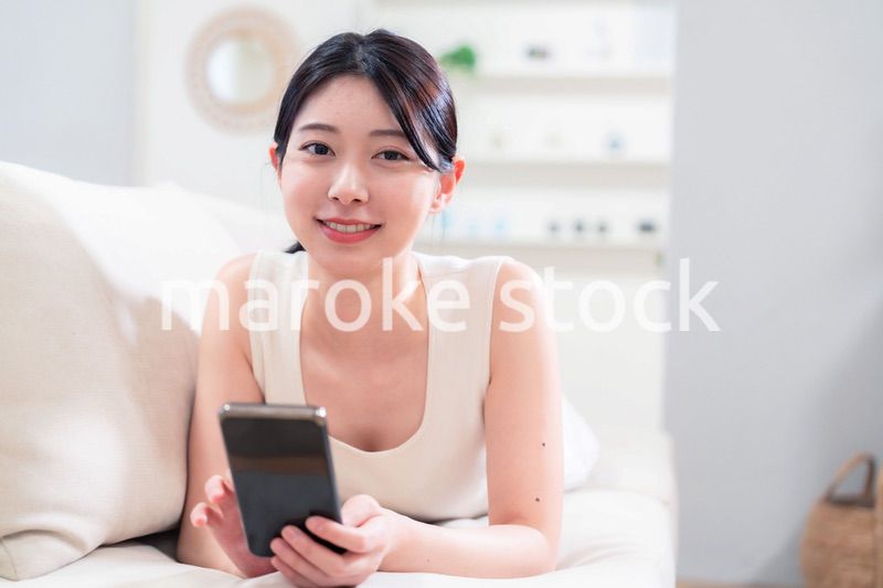 ソファで寝転がってスマホを使う若い女性