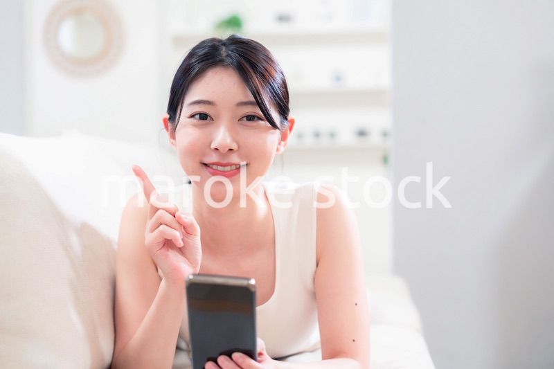ソファで寝転がってスマホを使う若い女性