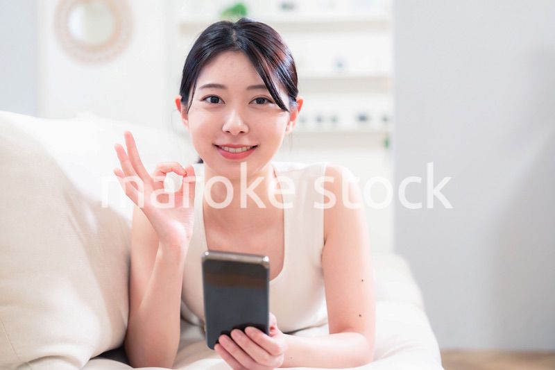 ソファで寝転がってスマホを使う若い女性