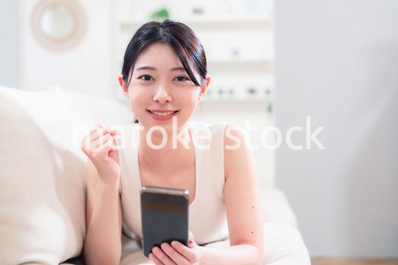 ソファで寝転がってスマホを使う若い女性