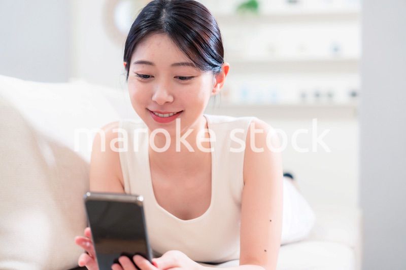 ソファで寝転がってスマホを使う若い女性