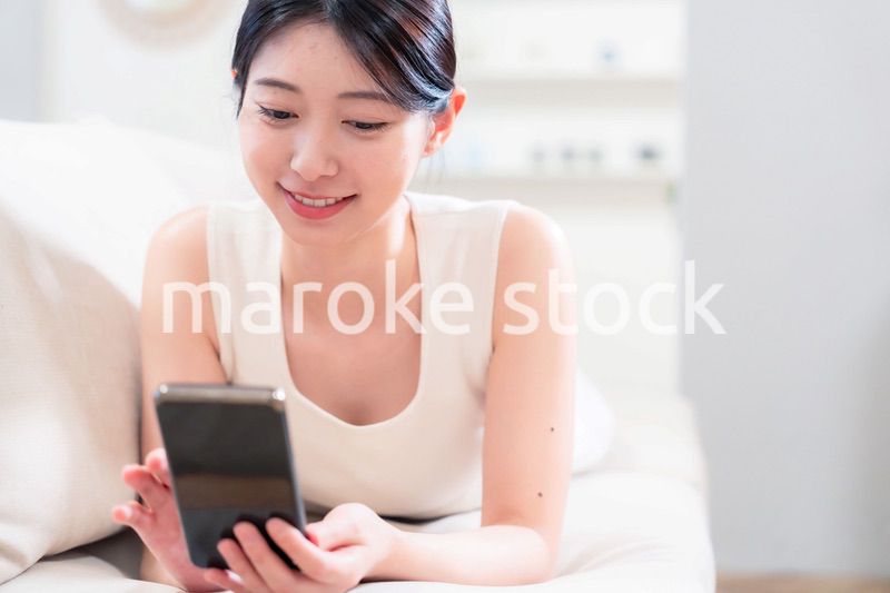 ソファで寝転がってスマホを使う若い女性