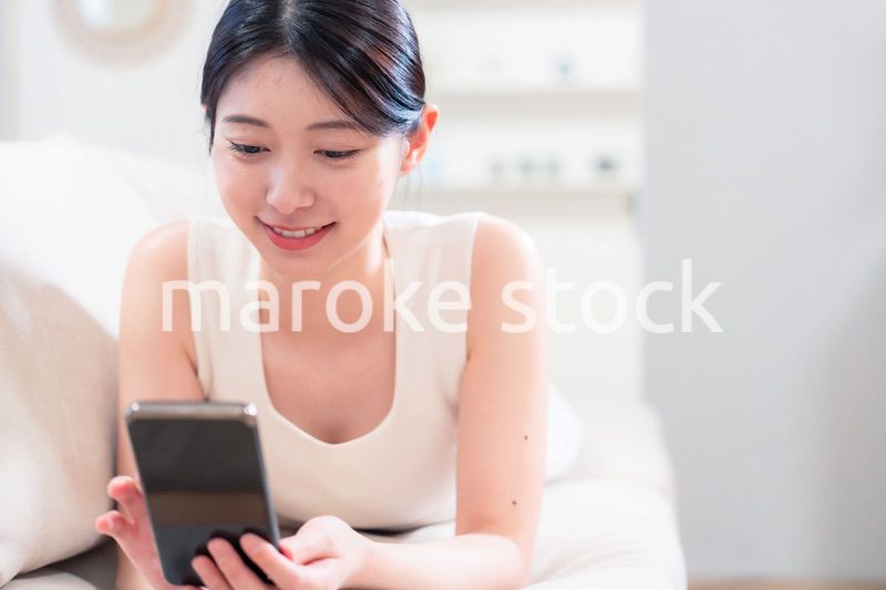 ソファで寝転がってスマホを使う若い女性
