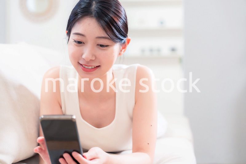 ソファで寝転がってスマホを使う若い女性