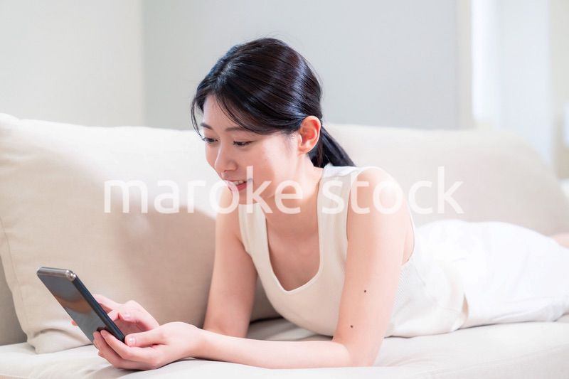 ソファで寝転がってスマホを使う若い女性