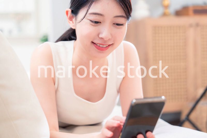 ソファで寝転がってスマホを使う若い女性