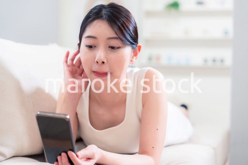 ソファで寝転がってスマホを使う若い女性
